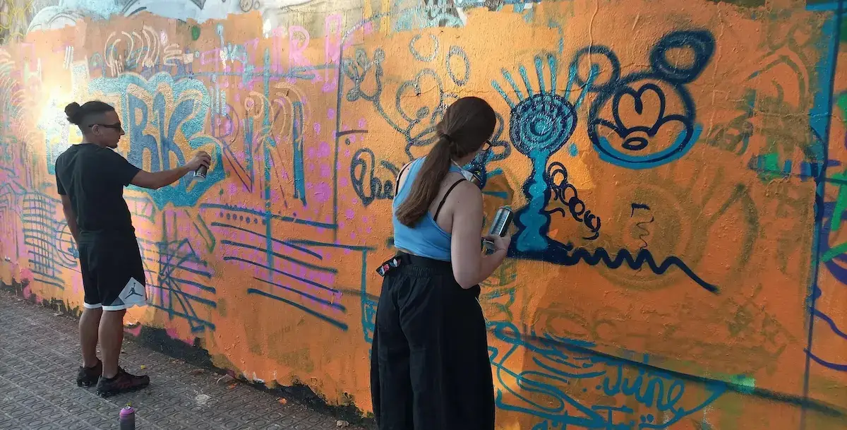 Alumnos pintando con spray sobre un muro en un curso de graffiti en exterior en Barcelona