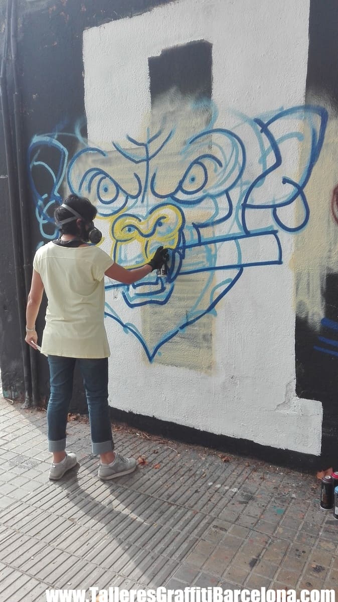 Participante con mascarilla pintando un diseño con contorno azul sobre una pared blanca