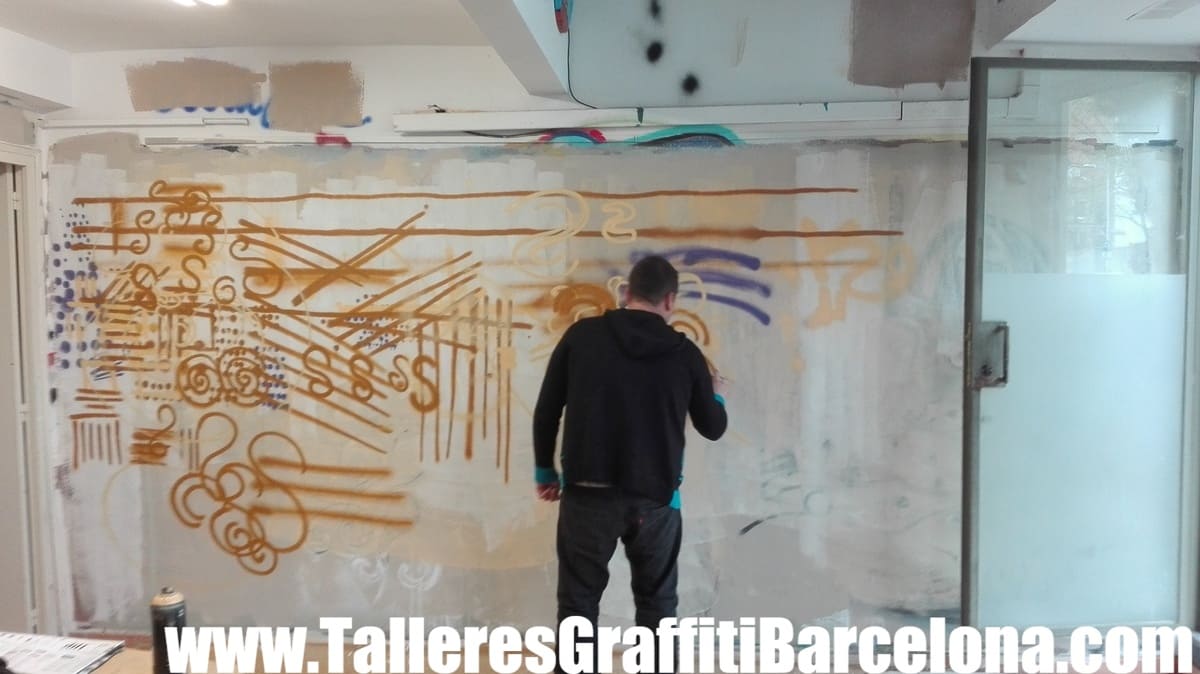 Participante pintando trazos dorados con spray sobre una pared blanca bajo un puente