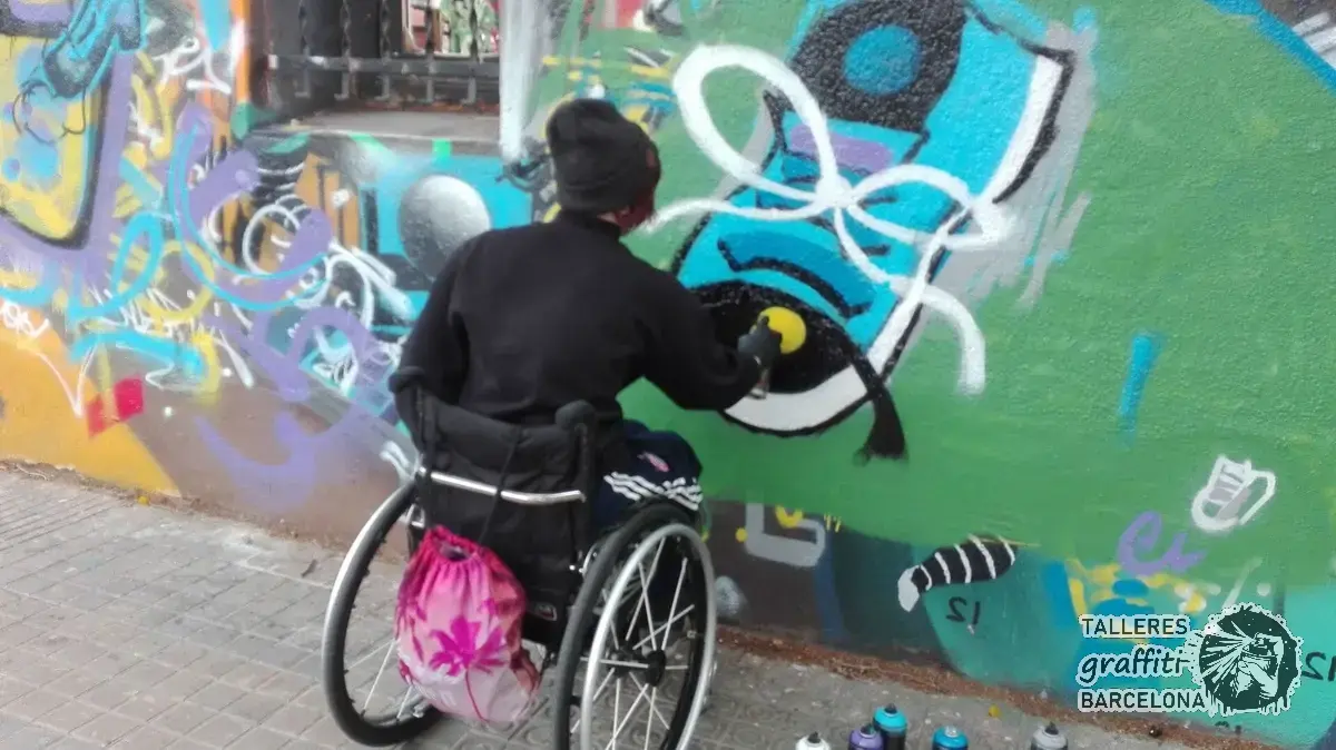 Participante en silla de ruedas pintando un graffiti azul y blanco sobre un muro de colores