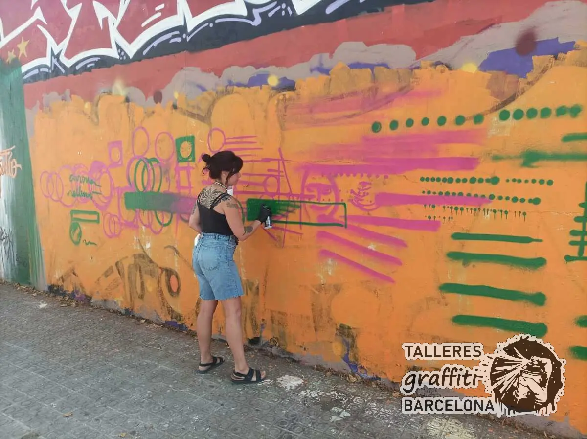 Participante pintando líneas rosas y verdes con spray sobre un muro naranja