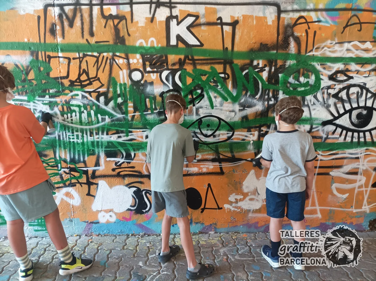 Adolescentes pintando graffiti con ojos y letras en un curso en Barcelona