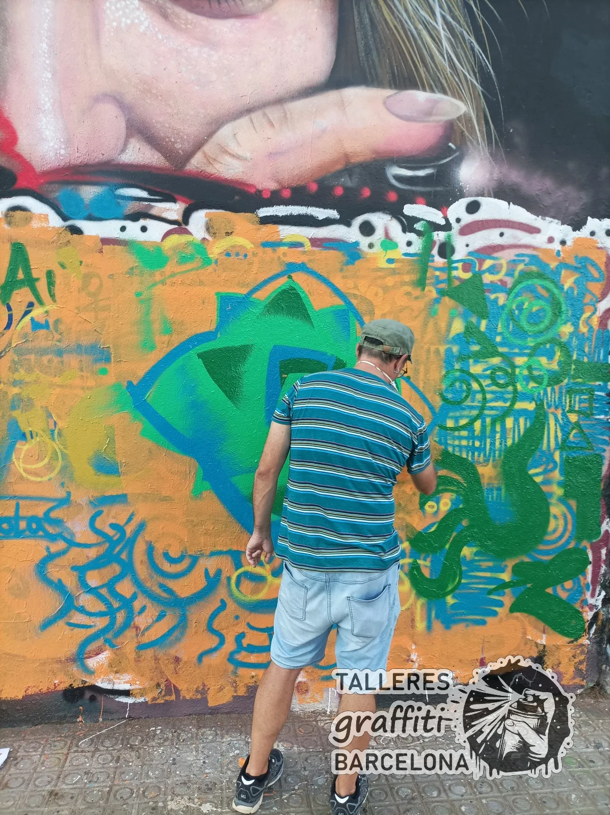 Participante pintando un diseño verde y azul sobre un muro naranja en un curso de graffiti en Barcelona