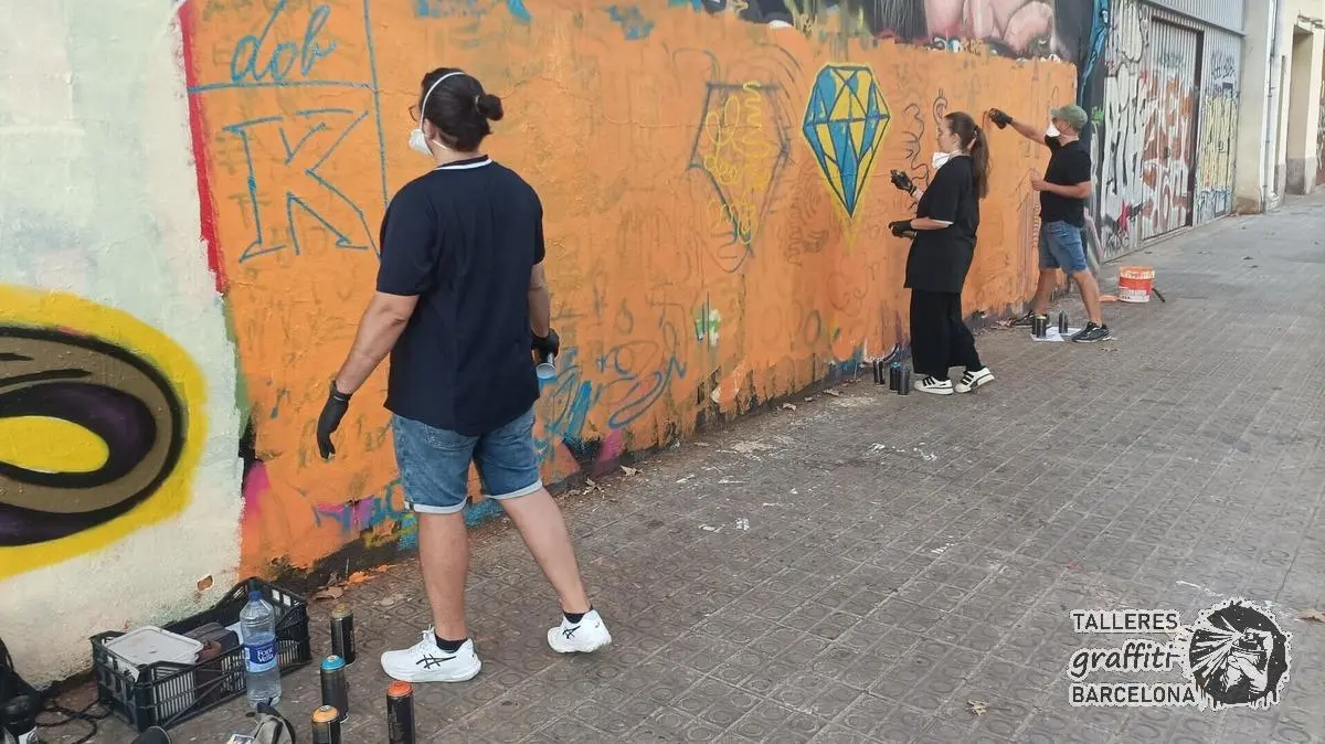 Participante con mascarilla pintando formas azules sobre un muro naranja